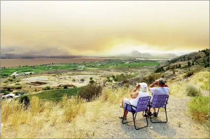  ?? MURRAY CHRUSCH/Special to The Herald ?? A couple seated on a hillside Tuesday morning above Osoyoos use binoculars to watch the Nk’Mip Creek fire, which has forced hundreds of people out of their homes.