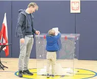  ??  ?? A man lets his son help him cast his ballot yesterday in Warsaw, Poland.