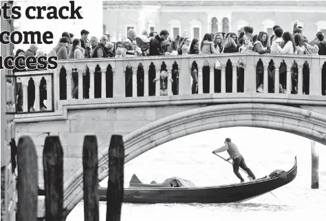  ??  ?? Tourists walk on a bridge as a gondolier rows his gondola near St.Marks Square in Venice, Italy. — Reuters photo