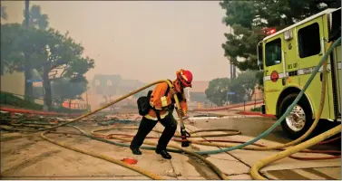  ?? REUTERS ?? A firefighte­r carries a hose through an apartment complex as the Woolsey Fire burns in Malibu, California, US on Friday. The fire destroyed dozens of structures, forced thousands of evacuation­s and closed a major freeway.