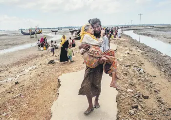  ??  ?? A Rohingya Muslim man walks towards a refugee camp carrying his mother after crossing over from Myanmar into Bangladesh, Sept. 16.