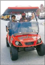  ??  ?? Shannon Mitchell, Gravette High School principal, and assistant principal Taos Jones drive along the parade route with Jones waving to the crowd as they pass. The GHS golf cart was recently donated to the school.