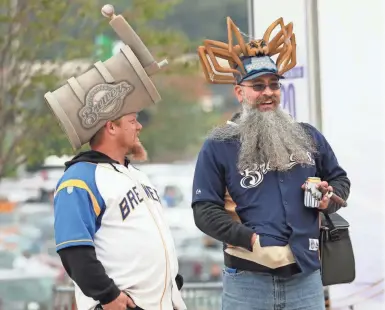  ?? MICHAEL SEARS / MILWAUKEE JOURNAL SENTINEL ?? Shawn Tucker wears a keg hat and Dan Davis dons a Fond du Lac Dock Spiders hat — a Northwoods League team based in Fond du Lac where both men are from. They were tailgating Friday before Milwaukee’s NLCS Game 1 win at Miller Park. More coverage in Sports and jsonline.com.