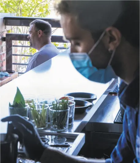  ?? Jessica Christian / The Chronicle ?? At Teleferic Barcelona in Walnut Creek, above, customers dine outdoors while bar manager Marc Pontavella (in mask and gloves) makes a cocktail; hand sanitizer greets guests, below, at an outdoor table at the Spanish restaurant. Left: Left Bank Brasserie’s patio in Larkspur is open to diners. Far left: Stephanie Light takes water to diners at the French restaurant in Larkspur.