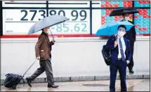  ?? ?? People pass in front of an electronic stock board showing Japan’s Nikkei 225 index at a securities firm in the rain Thursday, March 23, 2023, in Tokyo. (AP)