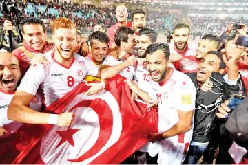  ??  ?? Players of the Tunisian national football team celebrate with their national flag after qualifying for the 2018 World Cup finals after winning their qualifiers match against Libya at the Rades Olympic Stadium in the capital Tunis on November 11, 2017....