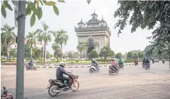  ??  ?? Motorcycli­sts ride around the Patuxai Victory monument in Vientiane.