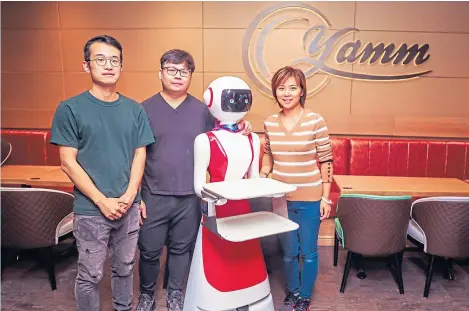  ??  ?? Restaurant managers Frank Ma and Kennt Chng with director Shan Gu and the new robot waiters.