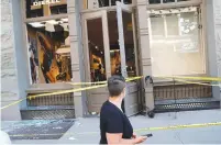  ?? (Mike Segar/Reuters) ?? A WOMAN walks past shattered windows of a Diesel store in Manhattan yesterday after it was looted and damaged.