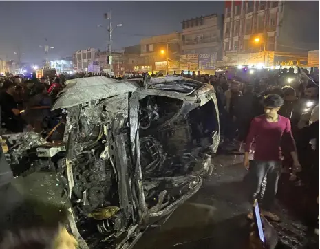  ?? AP ?? Iraqis gather near a destroyed vehicle after a US drone strike in eastern Baghdad late on Wednesday