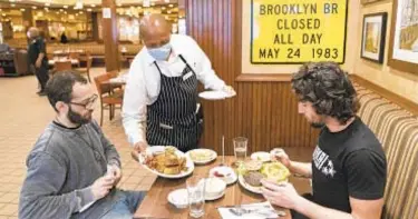  ?? MARK LENNIHAN | AP ?? David Zennario (left) and Alex Ecklin enjoy lunch indoors at Junior’s Restaurant in Brooklyn -- a luxury that soon might come to an end thanks to rising COVID-19 numbers.