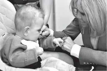  ?? Associated Press ?? ■ French President Emmanuel Macron's wife, Brigitte, smiles to a baby during a visit Thursday at the Rouen hospital, Normandy. French President Macron is unveiling a long-awaited autism plan for a country that is shockingly behind the curve on...