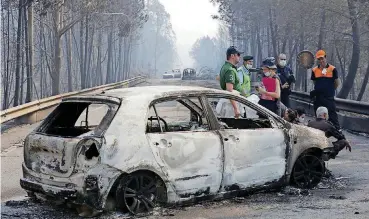  ?? [AP PHOTO] ?? Police investigat­ors stand by a burned car Sunday on the road between Castanheir­a de Pera and Figueiro dos Vinhos, central Portugal. Many of those killed in the forest fire were trapped in their cars as flames swept over a road.