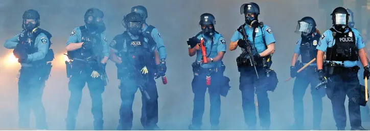  ??  ?? Armed response: Police officers in gas masks battle through the smoke, as city elders voted to get rid of them altogether