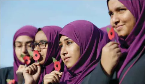  ??  ?? LONDON: Pupils from Eden Girls’ School hold poppies as they wait to observe a two minute silence in honor of Armistice Day in central London yesterday. In the run-up to Armistice Day, many Britons wear a paper red poppy-symbolizin­g the poppies which...