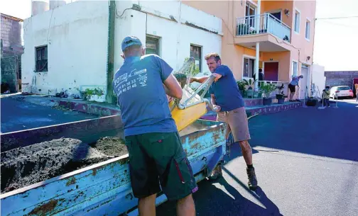  ?? EFE ?? Dos hombres limpian la ceniza acumulada a la entrada de una vivienda en Tazacorte