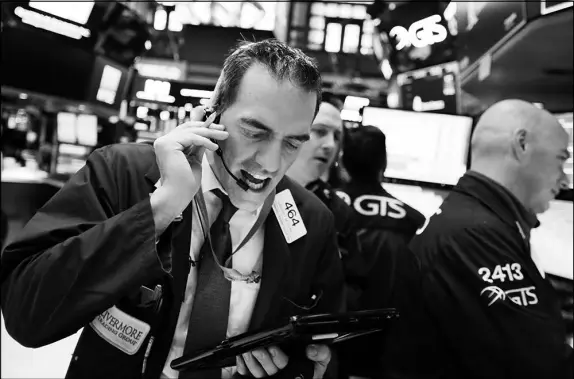  ?? RICHARD DREW / AP ?? Trader Gregory Rowe, left, works on the floor of the New York Stock Exchange on Monday. As the stock market becomes less predictabl­e, investors and traders prepare for wild rides.