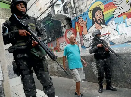  ?? GETTY IMAGES ?? A man walks past Brazilian Armed Forces soldiers as they patrol the Rocinha favela community in Rio de Janeiro after a spate of drug-related violence that has claimed at least four lives this week.