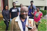  ?? AP PHOTO/ TED S. WARREN ?? Sophonie Bizimana, center, a permanent U. S. resident who is a refugee from Congo, poses Wednesday for a photo at his home in Kirkland, Wash., along with six of his children as he displays a cellphone photo of his wife, Ziporah Nyirahimby­a, who is in Uganda and has been unable so far to join him in the U. S.