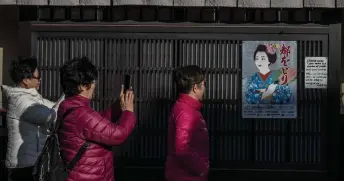  ?? — AFP photo ?? People take pictures of a poster of geisha in the Gion area of Kyoto.
