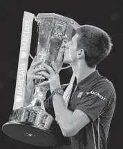  ?? — AFP ?? World no. 1 Novak Djokovic kisses the trophy after winning the ATP World Tour Finals in London on Sunday, following the withdrawal of Switzerlan­d’s Roger Federer from the final with an injury.