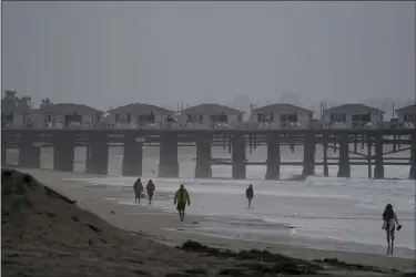  ?? GREGORY BULL — THE ASSOCIATED PRESS ?? People walk along a beach after hours of intense rain, March 21, in San Diego. California­ns are tired. Tired of the rain, tired of the snow, tired of stormy weather and the cold, relentless­ly gray skies that have clouded the Golden State nearly nonstop since late December.