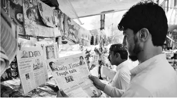  ??  ?? Pakistani residents read newspapers with a front page headline about Trump at a stall in Islamabad. — AFP photo