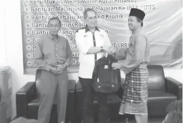  ??  ?? Wan Junaidi (centre) presents a school bag to school representa­tive.