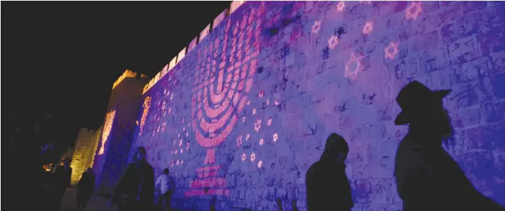  ?? (Reuters) ?? AN ORTHODOX man walks in front of a wall emblazoned with light during Israel’s celebratio­n of the liberation of Jerusalem. The public and Orthodox establishm­ent are often far apart on issues.