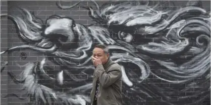  ??  ?? A man places his hand over his mouth as he walks past graffiti of a dragon on a street in Beijing yesterday. — AP
