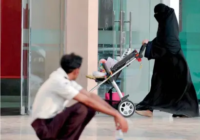  ?? AFP ?? A Saudi woman walks past a foreign worker at an entrance to a shopping mall in Riyadh. —