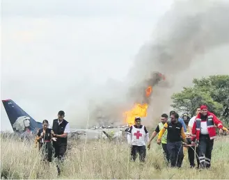  ?? RED CROSS DURANGO ?? Red Cross workers and rescuers carry an injured person on a stretcher, right, as airline workers, left, walk away from the site where an Aeromexico airliner crashed in a field in Durango, Mexico on Tuesday.