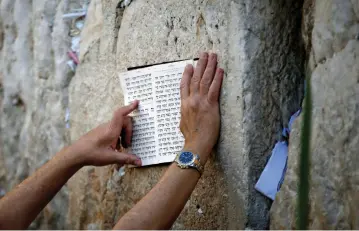 ??  ?? A JEWISH worshipper holds a religious script against the stones of the Western Wall.
