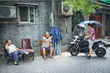  ?? LYU XIAOZHONG / FOR CHINA DAILY ?? An awning installed on a motorcycle gets the attention of a senior citizen in an alleyway in Beijing.