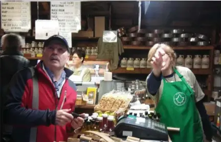  ?? ADAM DODD — THE NEWS-HERALD ?? A Burton Log Cabin clerk directs a customer toward different jars maple syrups on sale during the Geauga County village’s first Pancake Sunday of 2019.