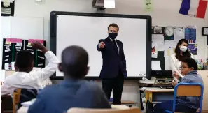  ?? Associated Press ?? ■ French President Emmanuel Macron wears a protective face mask as he speaks with schoolchil­dren during a class at the Pierre Ronsard elementary school Tuesday in Poissy, outside Paris. Starting May 11, all French businesses will be allowed to resume activity and schools will start gradually reopening.