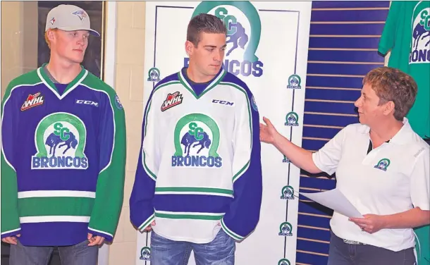  ?? Booster photo by Scott Anderson ?? Swift Current Broncos Assistant General Manager of Business Operations Dianne Sletten shows of some of the new design features on the new Bronco jerseys shown by Colby Cave and Justin Spagrud.