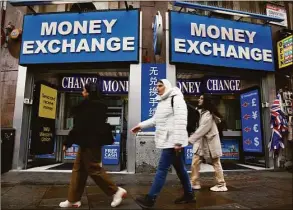  ?? David Cliff / Associated Press ?? People walk past a currency exchange bureau in London on Monday. The pound today slumped to its lowest level against the dollar since 1971, after the Chancellor hinted more tax cuts would follow those he announced last week. The pound dipped as low as $1.0349 per U.S. dollar early Monday but then rebounded to $1.0671, down 2.3 percent.