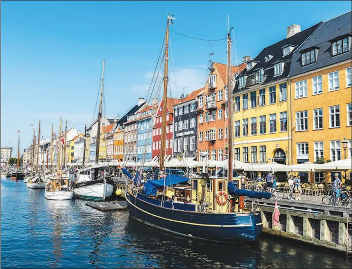  ?? SHUTTERSTO­CK PHOTOS (2019) ?? People drink at a terrace bar alongside old wooden sailboats moored along a canal in the Nyhavn district of Copenhagen, Denmark.