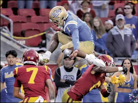  ?? Tribune News Service ?? UCLA quarterbac­k dorian Thompson-robinson hurdles high over USC safety Chase Williams, left, and cornerback isaac Taylor-stuart as he scores a touchdown on the play in the fourth quarter at Los Angeles Memorial Coliseum in Los Angeles on Saturday, Nov. 20, 2021. UCLA beat USC 62-33.