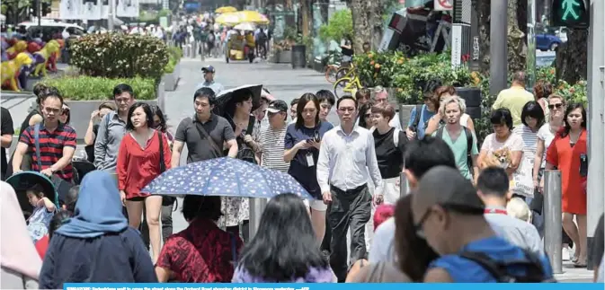  ?? —AFP ?? SINGAPORE: Pedestrian­s wait to cross the street along the Orchard Road shopping district in Singapore yesterday.