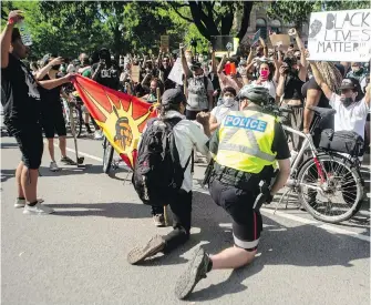  ??  ?? A police officer takes a knee with protesters as they gather outside the Ontario legislatur­e during an anti-racism rally in Toronto on Saturday.