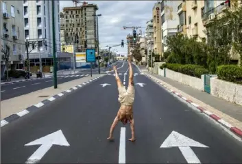  ?? Oded Balilty/Associated Press ?? An Israeli man stands on his hands on an empty road in Tel Aviv, Israel, Wednesday during a lockdown following government measures to help stop the spread of the new coronaviru­s.
