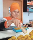  ?? JOURNAL SENTINEL RICK WOOD/MILWAUKEE ?? Indian Delight owner Arvinder Kaur places fresh sweets called laddo on a tray; sweets are displayed in a case and sold by weight.