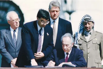  ?? ( Gary Hershorn/ Reuters) ?? THEN- FOREIGN MINISTER Shimon Peres ( sitting 2nd right) signs the Israeli- PLO peace accord as then- PLO chairman Yasser Arafat, thenprime minister Yitzhak Rabin and then- US president Bill Clinton stand behind him during a ceremony, at the White House in Washington, September 13, 1993.