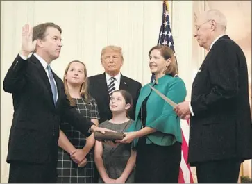  ?? Jim Watson AFP/Getty Images ?? BRETT KAVANAUGH, joined by his wife and daughters, is sworn in as a Supreme Court justice by retired Justice Anthony M. Kennedy at the White House. The eight other justices attended the ceremony.