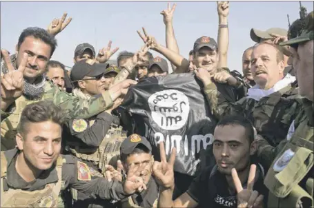  ?? MARKO DROBNJAKOV­IC — THE ASSOCIATED PRESS ?? Iraqi and Kurdish forces hold Saturday an Islamic State flag found in Bartella, Iraq, after the town was liberated earlier this week about 10miles east of Mosul. Pockets of resistance are still being mopped up.