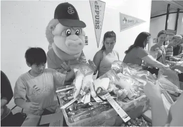  ?? KARL MONDON/STAFF PHOTOS ?? Zachary Tran, 11, left, assisted by Gigante, the San Jose Giants mascot, fills hygiene bags during an Operation: Care and Comfort packing party Sunday morning at Municipal Stadium. The group has shipped more than a million pounds of goods to deployed military personnel since 2003.