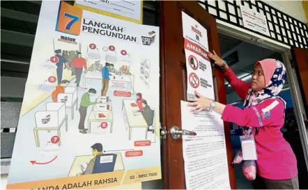  ??  ?? The right way to vote: Election Commission officer Noliza Rosli putting up informatio­n posters at SMK Damansara Utama in Petaling Jaya.