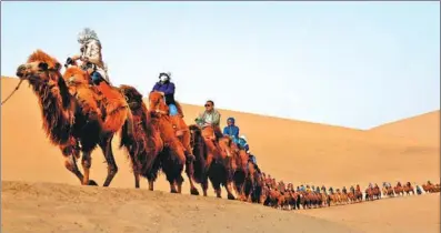  ?? ZHANG XIAOLIANG / XINHUA ?? Tourists cross the sand dunes of Mingsha Mountain and Crescent Moon Spring scenic area in Dunhuang, Gansu province, in April. The city was visited more than 9 million times last year.